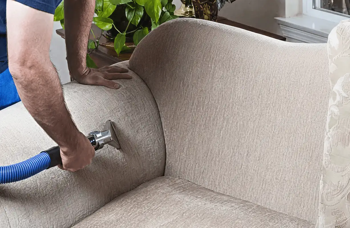 Professional upholstery cleaner deep-cleaning a fabric sofa with a handheld extraction tool and hose, Boise, ID.